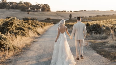 a bride and groom walking down a dirt road during sunset at Coriole Winery
