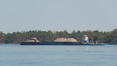 A tugboat pushes a large barge loaded with piles of sand.