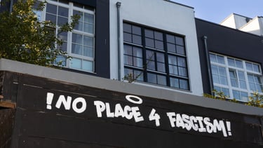 Bild von schwarzen und weißen Häusern, im Vordergrund ist das Graffitti "No room for facism".