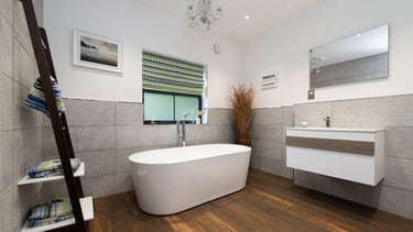 A luxury bathroom with wooden floors and grey tiles. A freestanding bath is the main feature.