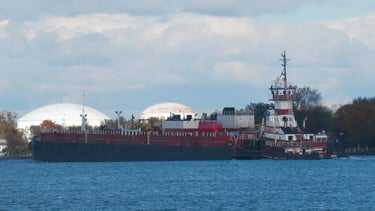 A stern view of tugboat Albert pushing barge Margaret past an industrial facility.