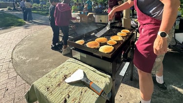 Kids in the background of a person flipping pancakes on a griddle in a park