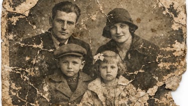 A damaged vintage family portrait showing a mother, father, and two children in early 20th-century attire.
