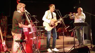 Joël Royer au centre de la scène joue de la guitare sèche avec contrebasse et flûte traversière