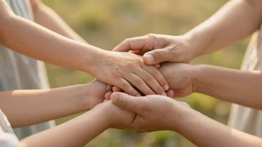 Warm editorial photography of multi-generational family hands gently holding each other, soft golden hour light, shallow depth of field, serene natural background
