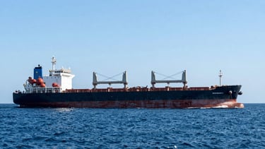 Wide environmental shot of a massive bulk carrier vessel underway in deep blue ocean water under clear bright skies
