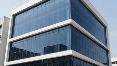 A professional photography shot of a sleek, modern commercial building in Bandung, Indonesia, with large glass windows covered in premium dark privacy film. The setting is Southeast Asian urban environment during a bright clear day, emphasizing the clean architectural lines and the efficient reflection of the innovative window solution. The image uses a palette of white and dark blue.