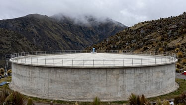 Wide shot of a clean concrete water storage tank in the green Andean highlands of Tasco, misty paramo mountains in the background, overcast natural daylight.