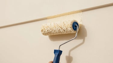 Close-up of a pristine paint roller applying warm cream paint to a smooth wall, perfect clean-cut lines, bright natural daylight, minimalist architectural detail