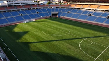 High-contrast aerial drone photography of a modern sports park in Eagle Mountain Utah, sharp white field markings on vibrant green turf, dramatic late afternoon sun casting long shadows, 35mm