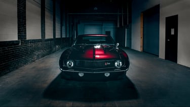 Front view of a classic red and black Chevrolet Camaro Z28 parked in a dark industrial garage.