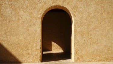 Warm editorial photograph of a rustic Mallorcan interior, sunlight streaming through an open arched doorway, lime-washed walls, minimalist aesthetic.