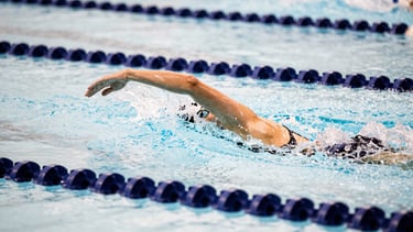 High-speed shutter shot of a swimmer's hand fending through crisp water, frozen droplets, deep navy lane lines, high contrast indoor pool lighting, 35mm