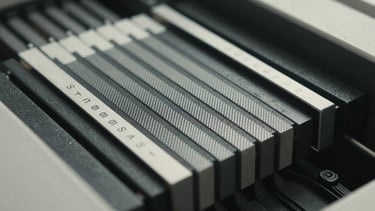 Extreme close-up of a printing press colour separation bar with registration marks, halftone dot pattern visible under bright north-facing daylight, flat documentary framing, ink-black press surface