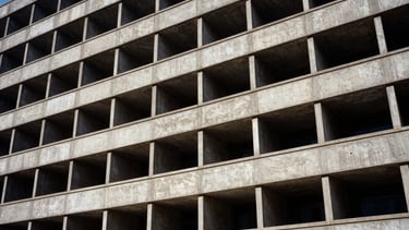 Wide panoramic view of a brutalist building facade, harsh direct sunlight creating deep shadows, strict orthogonal lines, architectural film photography, 35mm lens.