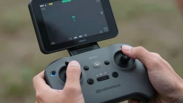 A close-up of a drone pilot's hands operating a professional controller with a high-brightness monitor. The setting is outdoors and professional. Cinematic lighting.