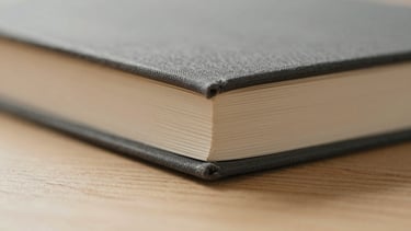 Macro photograph of a minimalist book spine, textured charcoal fabric cover, exposed binding details, resting on a light oak surface, soft morning side-light, shallow depth of field