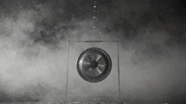 Surreal monochrome 35mm photography of water droplets suspended mid-air, floating upward towards a dark sky, a silent metal gong hovering in the misty background, high contrast ink-wash tones, ethereal diffused mist-light