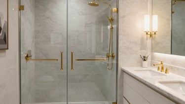 A luxury bathroom interior in a North American home featuring a large walk-in shower with soft gray tiling and gold fixtures. A sleek double vanity with white marble countertops sits under warm, elegant lighting. The composition is professional and modern, using a palette of white, light gray, and gold accents to convey a sense of high-end craftsmanship.