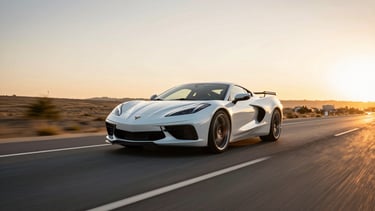 Wide panoramic shot of a white sports car in motion on an empty two-lane road at golden hour, motion blur on background landscape, car sharp and centered low in frame, warm horizon light raking across the hood