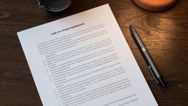 Top-down candid shot of a script and a charcoal pen on a dark wooden table, terracotta lighting from a nearby lamp. North American office.