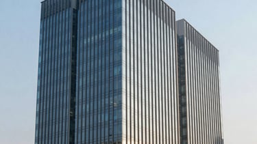A professional architectural photograph of a modern steel and glass corporate building in a business district of North India. The lighting is early morning with soft steel blue reflections on the windows and a clean, light blue sky. Professional corporate environment with South Asian / Indian urban context.
