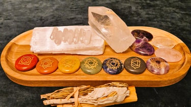 A variety of crystals placed on a wooden tray, with bundle of palo santo, sage and rosemary in front