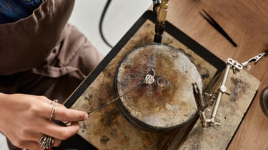 Un joyero usa un soplete para soldar un anillo de plata en un banco de trabajo dentro de un taller