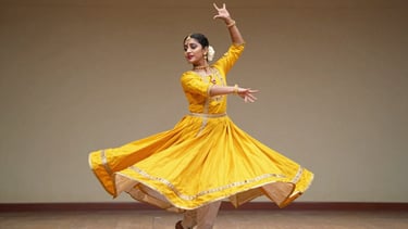 Candid capture of a Kathak dancer spinning gracefully, marigold dress swirling, warm stage lighting, video play overlay.