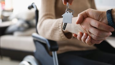 A participant in a wheelchair holding being assisted for better independence