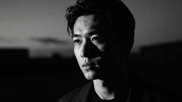 High-contrast portrait of the artist in shadow, deep twilight, 35mm anamorphic lens, cinematic film photography, dramatic chiaroscuro lighting.