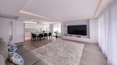 Modern open-plan living room and white kitchen with a large rug, sofa, and wall-mounted TV.