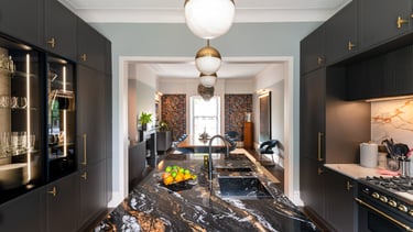 Modern luxury kitchen featuring a black marble island, dark grey cabinets, and gold accents.