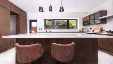 Modern luxury kitchen with dark wood cabinets, white quartz island, and leather bar stools.