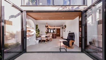 Modern open-plan living room and kitchen featuring large black bi-fold glass doors opening to a patio.