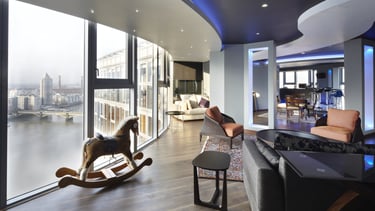 Modern luxury penthouse living room with floor-to-ceiling windows overlooking a river and city skyline.
