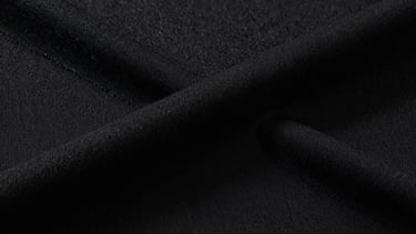 Extreme close-up of heavy-weight black cotton fabric weave, sharp directional studio lighting revealing the coarse, premium texture and thick structural seams.