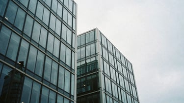 Low-angle architectural crop of a modern glass office building in London under cool overcast daylight, sharp contrast, 35mm film grain