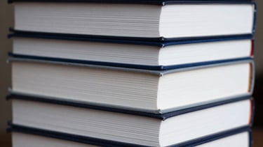 A stack of various professionally published books showing diverse spine designs in shades of white and navy blue.