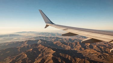 Wide panoramic view of an airplane wing over a vast alpine landscape, clear blue sky, crisp detail, warm editorial photography