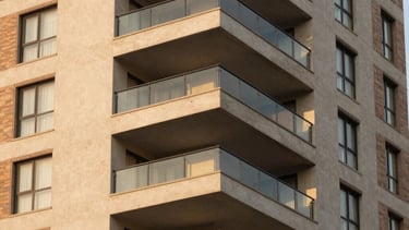 Professional architectural photography of a luxury apartment building in the Cidade Nova neighborhood of Belo Horizonte, Brazil. The image showcases the modern balcony of a penthouse with clean lines and glass railings. Warm golden hour light reflects off the windows, highlighting the sophisticated light beige and muted brown textures of the facade. South American / Brazilian setting.