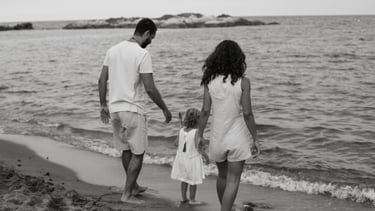 Black and white photo of a family walking along a sandy beach near the ocean waves.