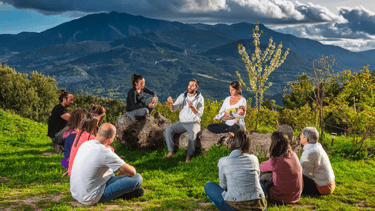 A group of people sitting in a mountain landscape during an outdoor wellness retreat session.