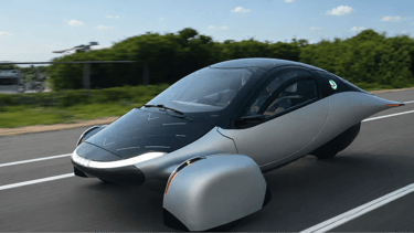 Aptera Solar EV rodando em rodovia durante o dia com carroceria aerodinâmica e painéis solares