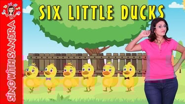 a woman in a pink shirt and jeans standing in front of a fence and six little ducks
