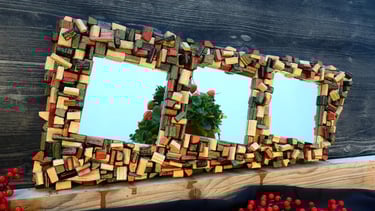 Elegantes Spiegelunikat mit kunstvollem Rahmen aus schwarzen, roten, goldenen und grünen Holzscheiten