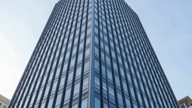 A low-angle, architectural photograph of a contemporary commercial real estate skyscraper in a North American business district. The building features clean glass lines and steel blue frames. The lighting is bright, clear daylight, reflecting a sophisticated and trustworthy corporate environment. Professional and sharp composition.