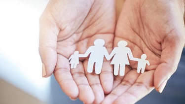 Manos sosteniendo figuras de papel de una familia, simbolizando Derecho de Familia.