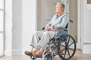 Elderly man in wheelchair looking out window in bright, peaceful home setting