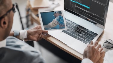 Four small, white robot figures are sitting in a row, each with a laptop in front of them. They have round bodies and blue accents, with 'AI' displayed on their chests. The background is minimal and light gray, emphasizing the robots and their computers.
